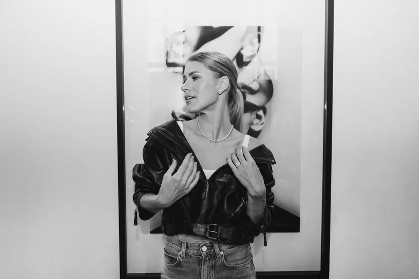 Black and white portrait in a leather jacket and a diamond necklace, before a framed photograph
