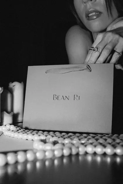 A gold-stamped Bean Ri bag beside loose pearls in candlelight
